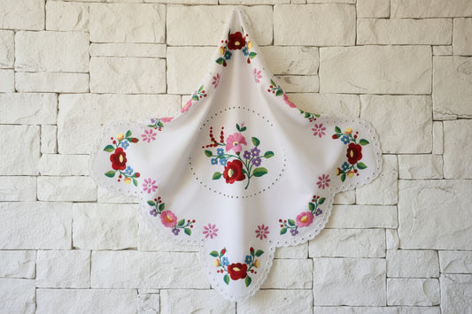 Χειροποίητο τετράγωνο εργόχειρο  στεφάνι45x45 εκ. με πολύχρωμα παραδοσιακά κεντητά λουλούδια σε λευκό βαμβακερό ύφασμασε πετρινο τοίχο