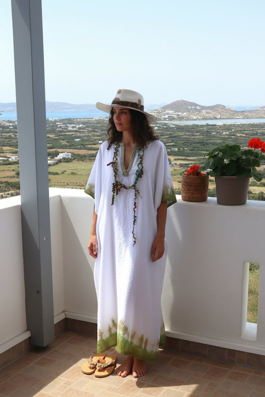 καφτάνι λινο  μακρι λευκό με ζωγραφικη και κολιε χειροποιητο και σανδαλια δερματια σε μοντέλο σε βεράντα και καπέλο mousses greek art
